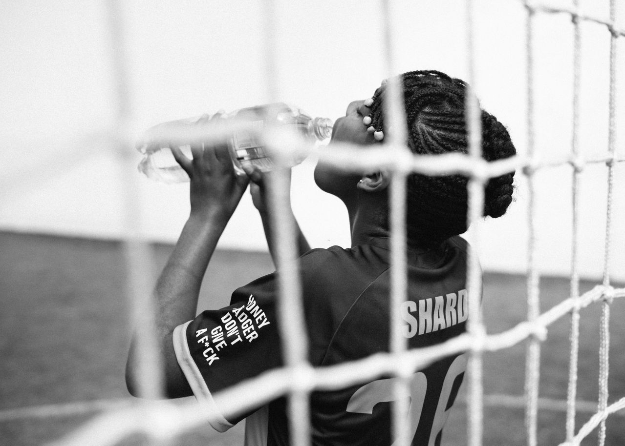 A young player drinking water in the shade during an evening training break