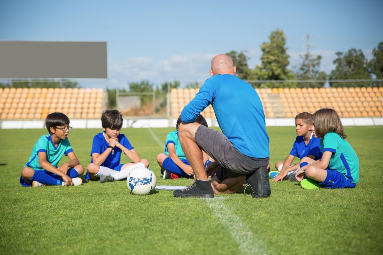 Kids in bibs dribbling through cones at a summer soccer camp on a green field